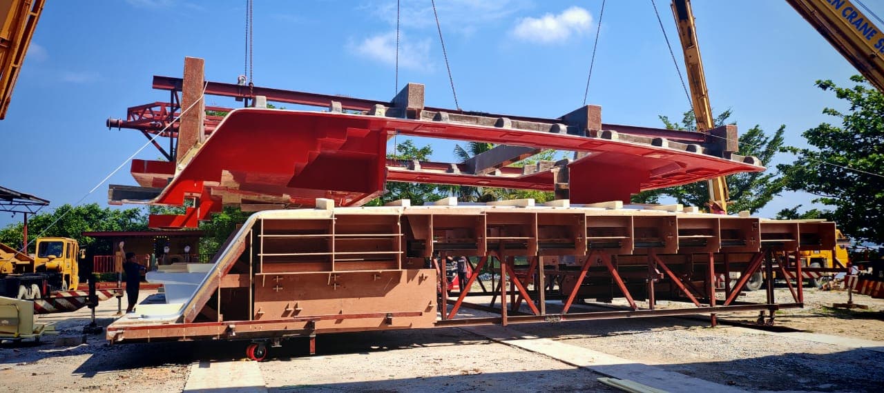 Catamaran hull and red mold being lifted at the yard